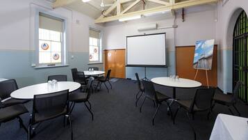 A conference room with round tables and chairs, a whiteboard, and a projector screen.