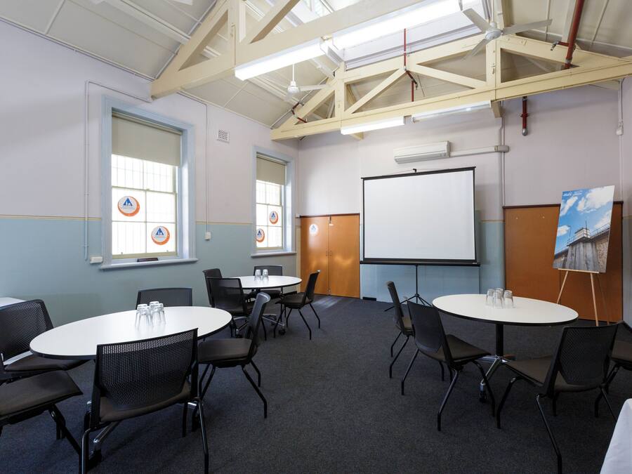 Een congreszaal met ronde tafels en stoelen, een whiteboard en een projectiescherm.