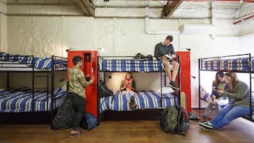 Une chambre de dortoir avec des lits superposés, un plancher en bois et une armoire rouge.