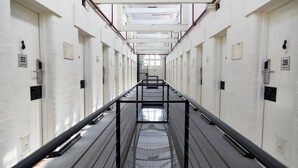 A corridor with white walls, numbered doors, and a metal railing. - YHA Fremantle Prison (Fremantle)