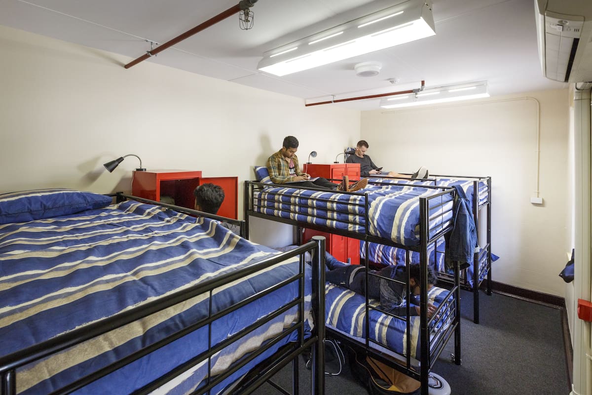 Une chambre de dortoir avec des lits superposés, un bureau et une armoire rouge.