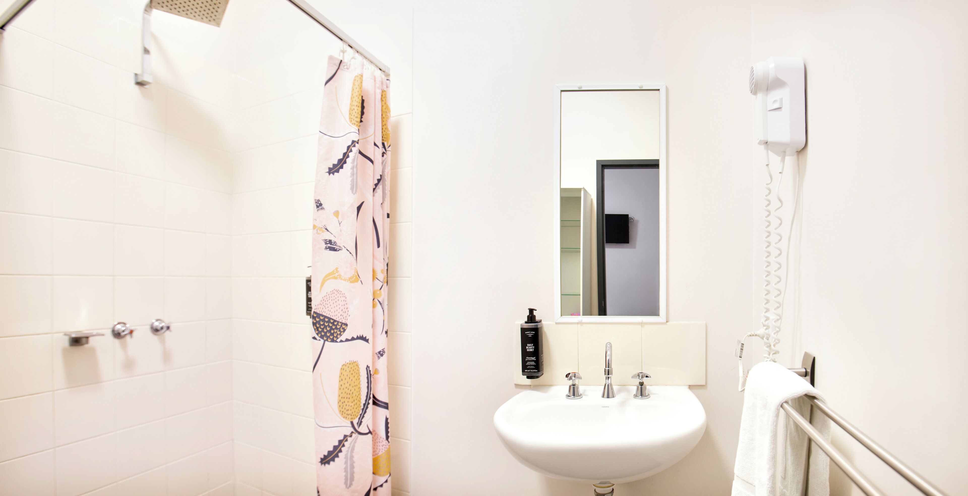 A bathroom with a shower, a sink, a mirror, and a hairdryer on the wall.