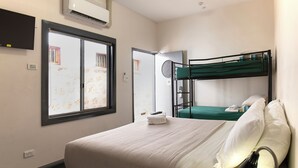 A hotel room with a single bed, a bunk bed, a TV, an air conditioner, and a window with a view. - YHA Fremantle Prison (Fremantle)