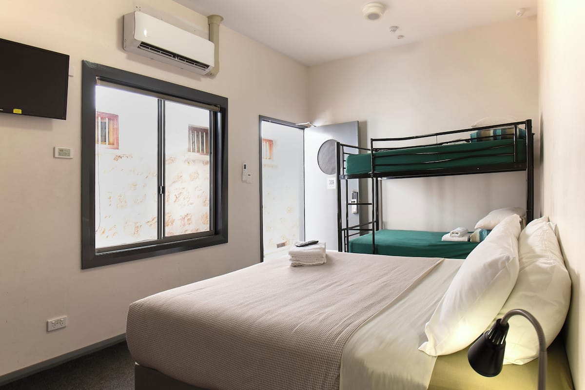 Une chambre d’hôtel avec un lit simple, un lit superposé, une télévision, la climatisation et une fenêtre avec vue.