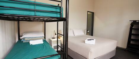 A hotel room with a bunk bed, a single bed, a bedside table with a lamp, and a mirror on the wall.