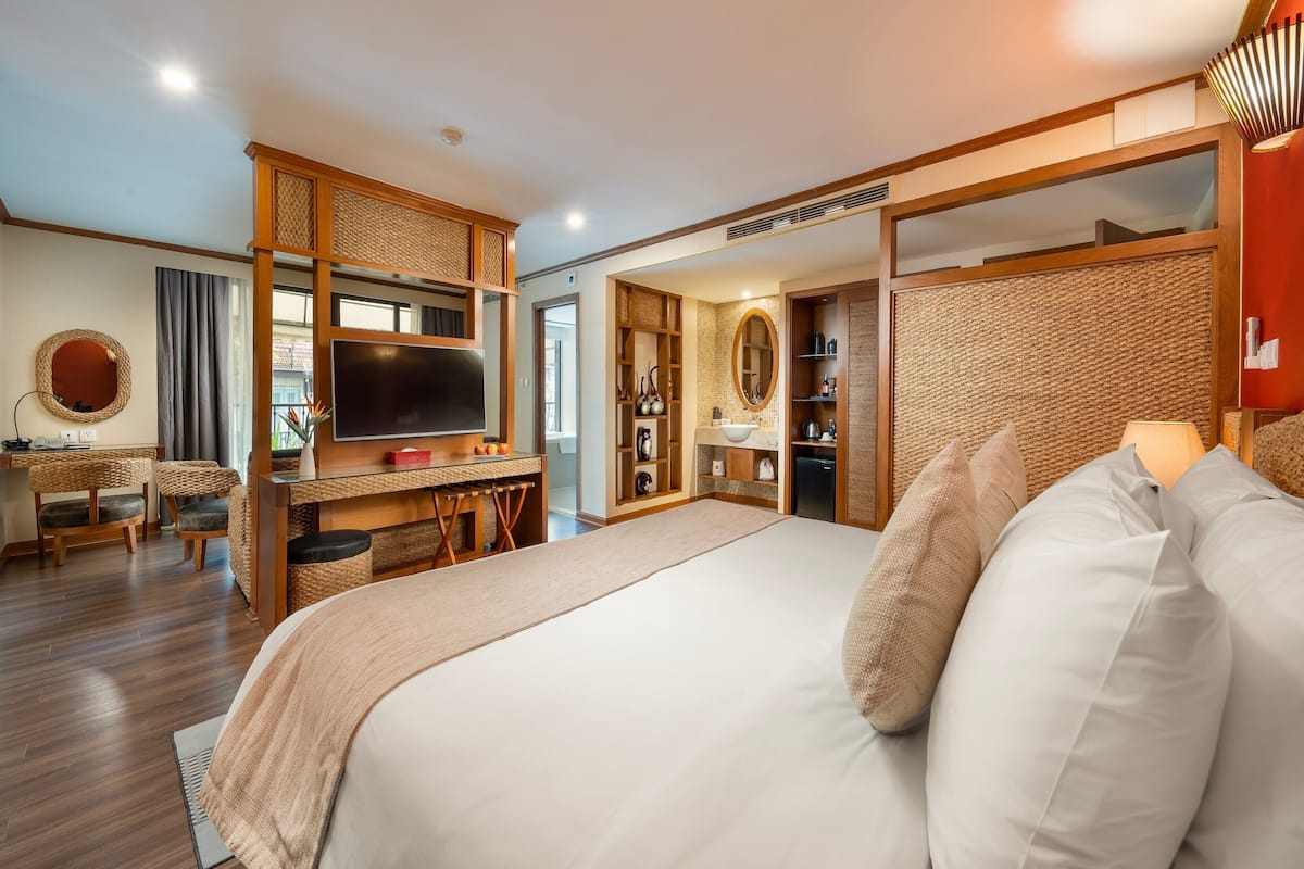 Habitación de hotel moderna con una cama grande, un escritorio con televisión de pantalla plana, un armario y un baño visible a través de una puerta abierta.