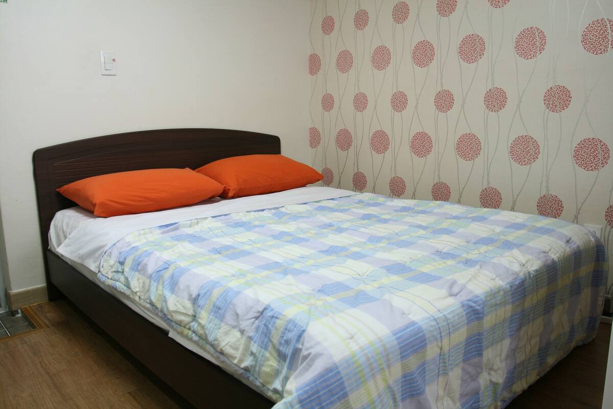 A bed with an orange pillow, a plaid bedspread, and a wall with a circular pattern.