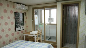 Habitación de hotel con cama, escritorio con silla, zona de ducha y ventana con mosquitera.