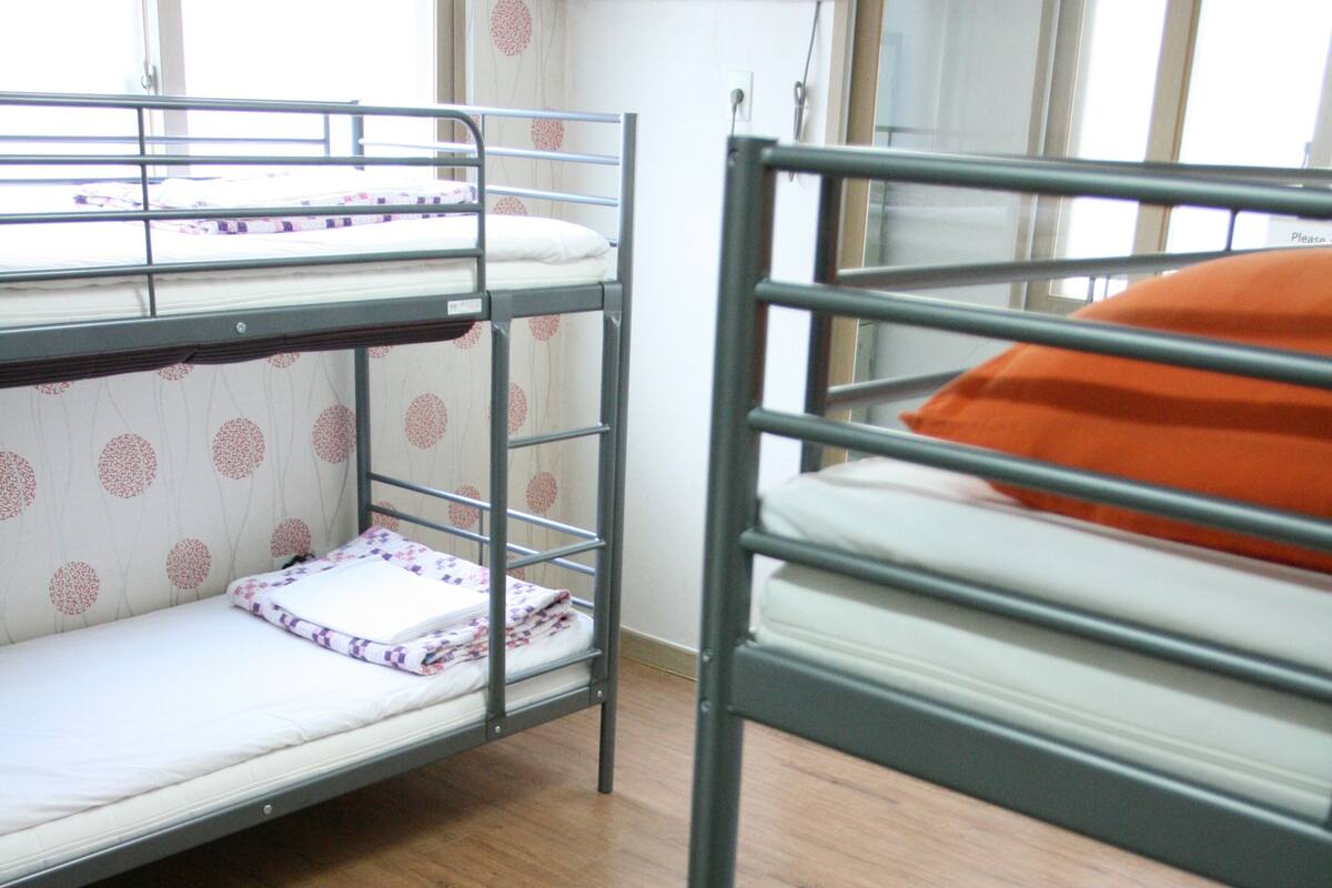 A bunk bed room with a window, wooden flooring, and an air conditioning unit on the wall.
