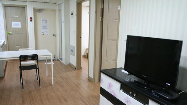 Habitación de hotel con televisor de pantalla plana, una mesa de comedor con sillas y un área de kitchenette.