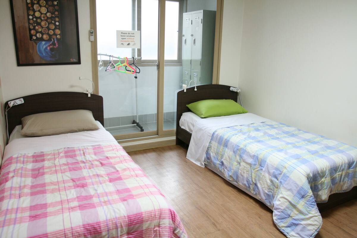 A bedroom with two beds, a shower area, and a view of the outside.