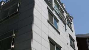 Un edificio de varios pisos con un estilo arquitectónico moderno, que presenta una fachada plana, ventanas amplias y una escalera contra incendios visible en el lado izquierdo.