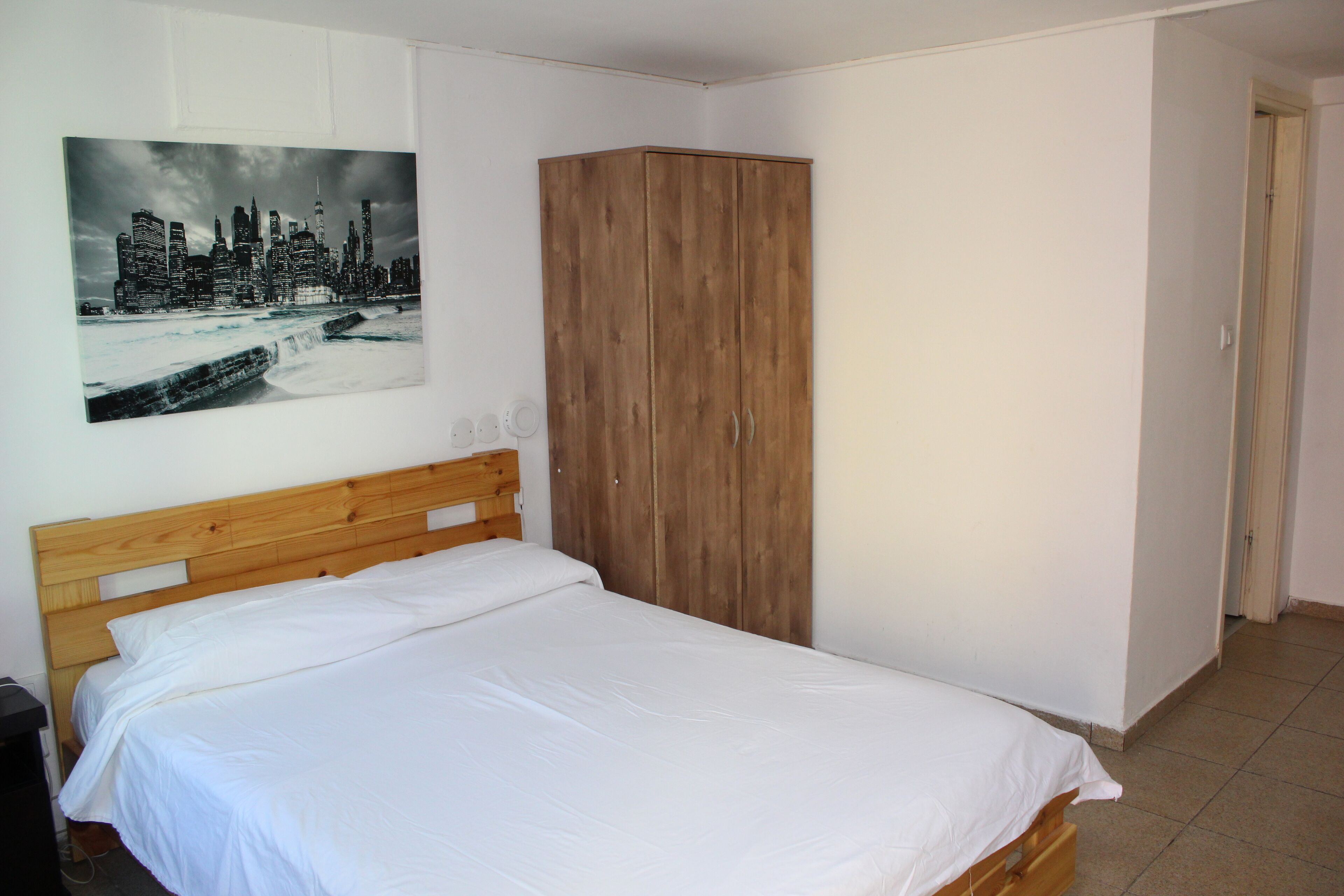 A bedroom with a wooden bed, a wardrobe, and a cityscape painting on the wall.