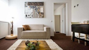 Una sala de estar con un sofá beige, una mesa de centro de madera con objetos decorativos, una obra de arte con temática de cebra en la pared y un piano al fondo.