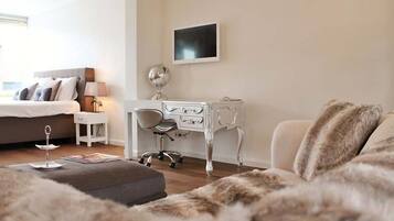 Een moderne slaapkamer met een bed, nachtkastje, lamp, bureau, stoel en een televisie.