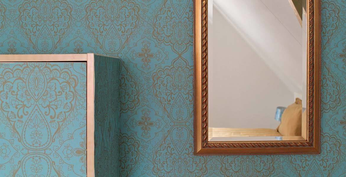 Una habitación con papel tapiz estampado y un espejo con marco dorado.