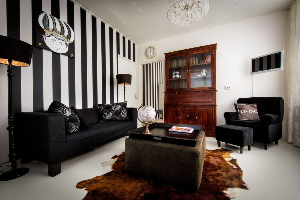 A living room with a black and white striped wall, a globe on a coffee table, a wooden cabinet, and a black armchair with a pillow labeled "LIVING".
