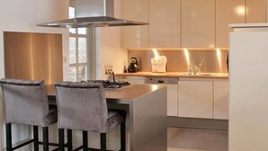 Una cocina moderna con una isla central, dos taburetes de bar, una estufa a gas, un hervidor y un lavavajillas.