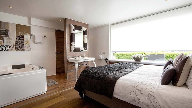 Un dormitorio moderno con una cama grande, un tocador con espejo y una ventana con vistas a zonas verdes.