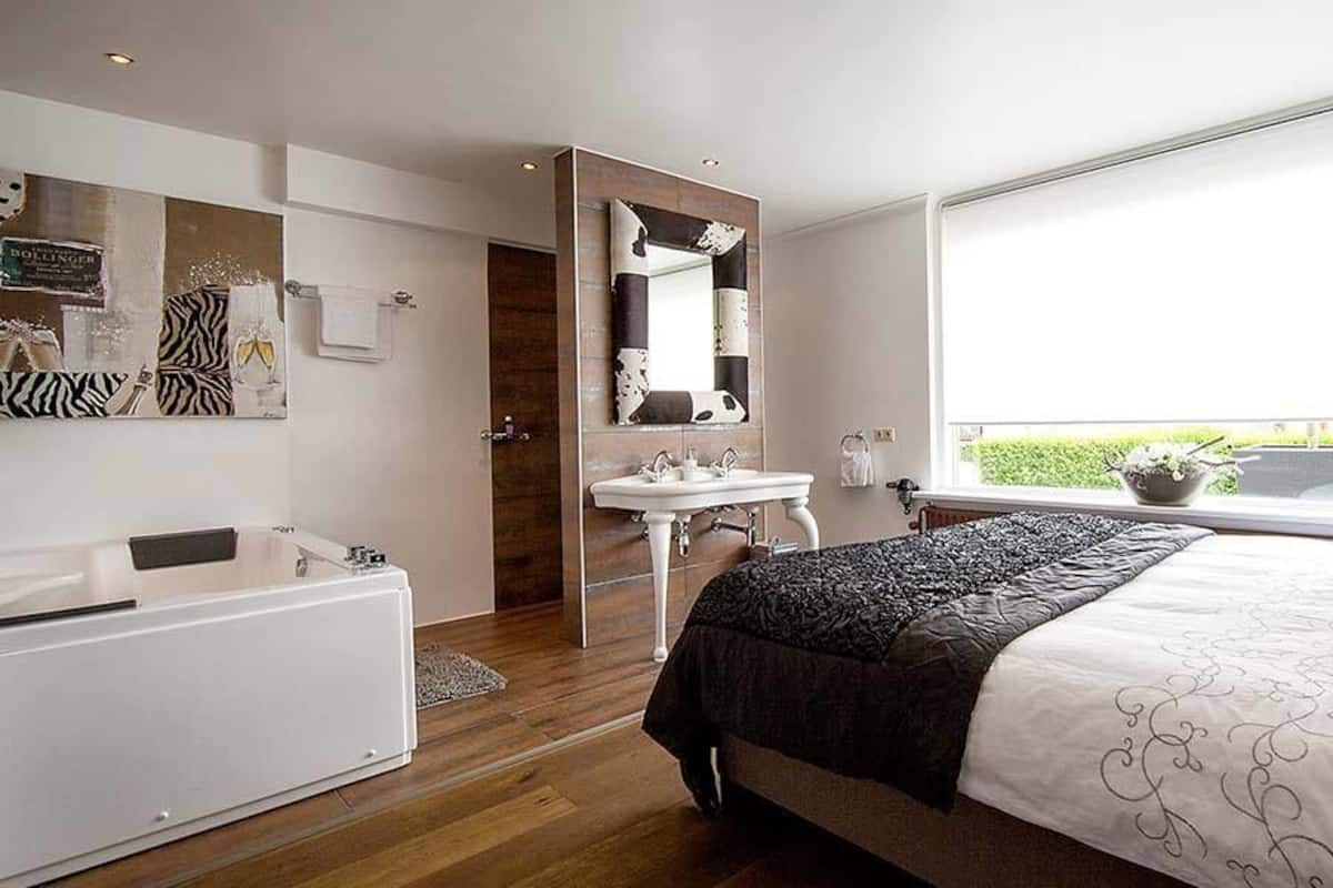 A modern bedroom with a large bed, a vanity with a mirror, and a window with a view of greenery.