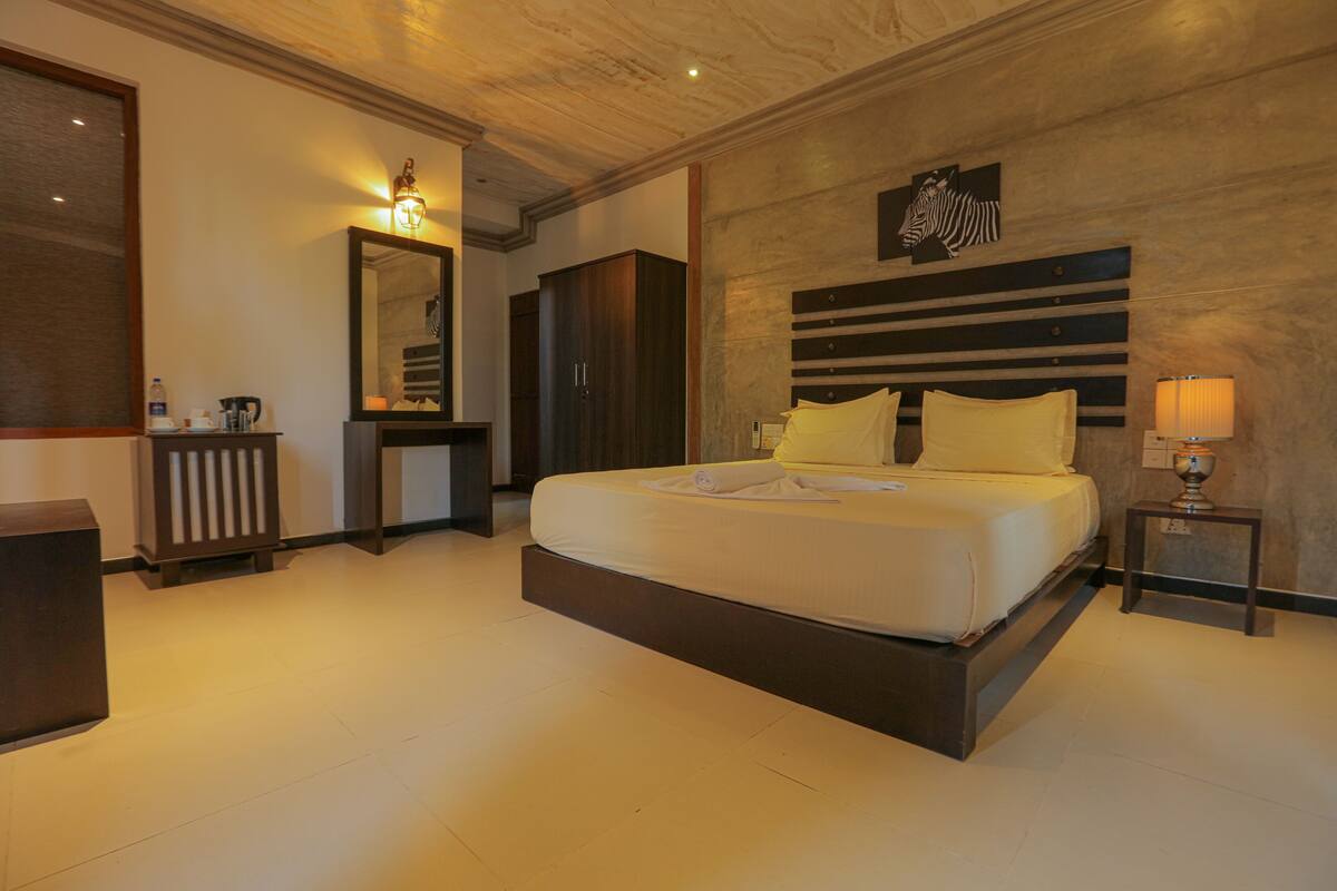 A hotel room with a large bed, a bedside table with a lamp, a mirror, a wardrobe, and a zebra artwork on the wall.
