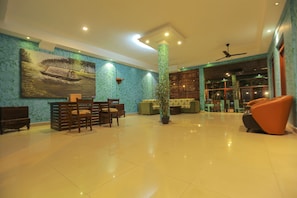 A spacious lobby with a dining area, a large painting, a potted plant, and a ceiling fan.