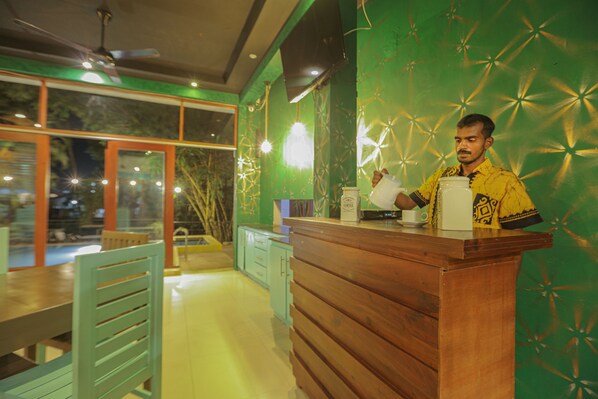 A reception desk with a wooden counter, a person standing behind it, and a green patterned wall.