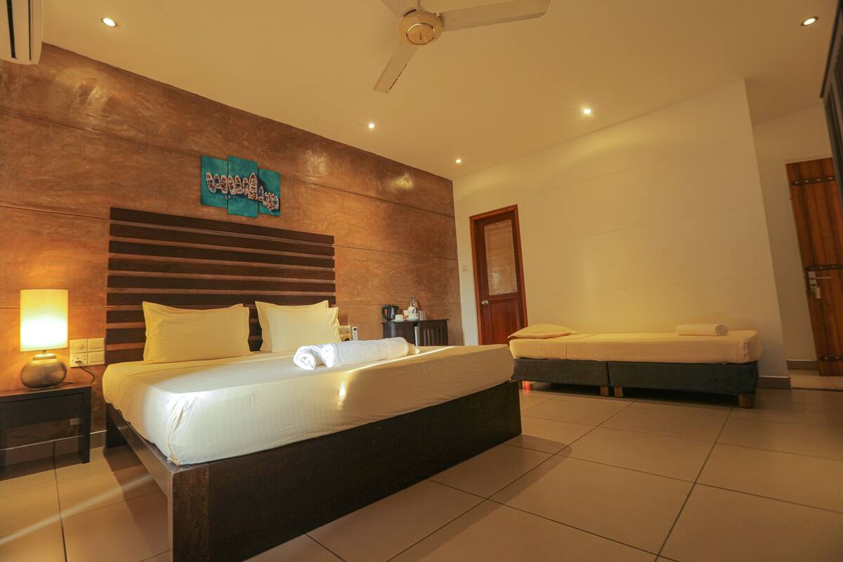 A hotel room with a large bed, a smaller bed, a nightstand with a lamp, and a wooden headboard.