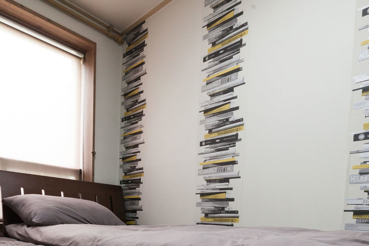 Une chambre à coucher avec un lit, une fenêtre et un mur décoré de livres.