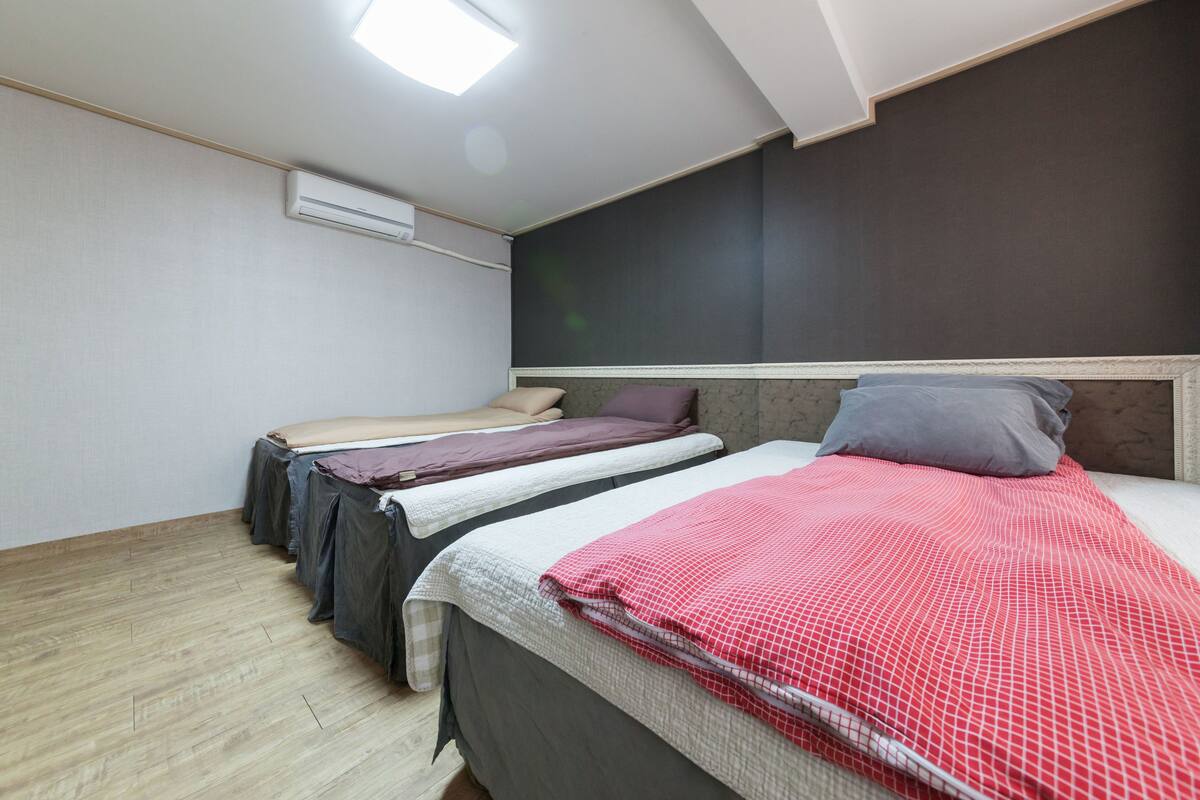Une chambre avec trois lits, un ventilateur de plafond et une fenêtre.