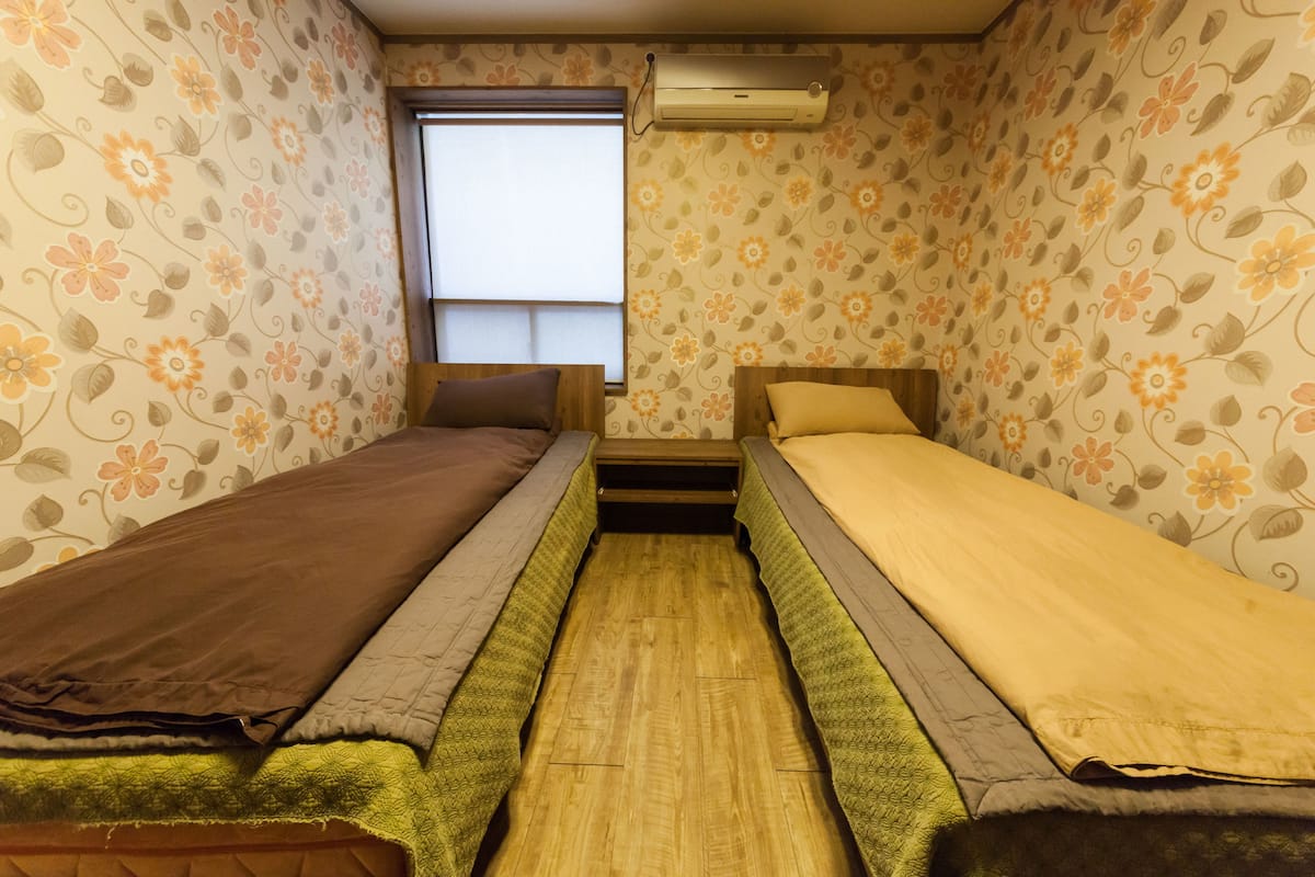 Une petite chambre avec deux lits simples, une fenêtre et un appareil de climatisation.