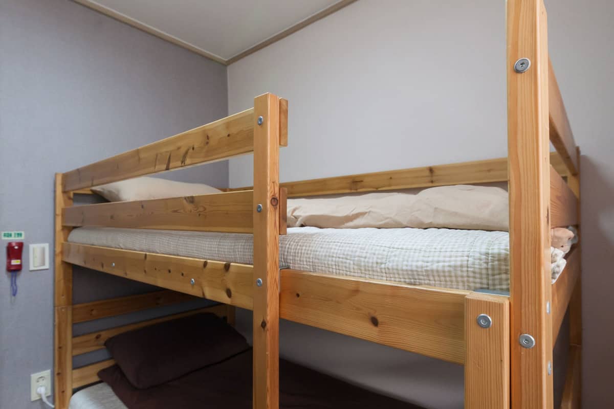 Un lit superposé dans une pièce dont le sol est en bois et où se trouve un interrupteur sur le mur.