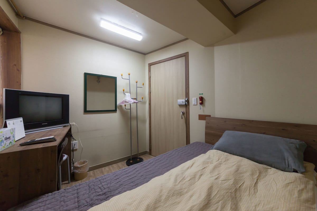 Une chambre d’hôtel avec un lit, un bureau avec une télévision, un miroir, une porte et une lampe de sol.