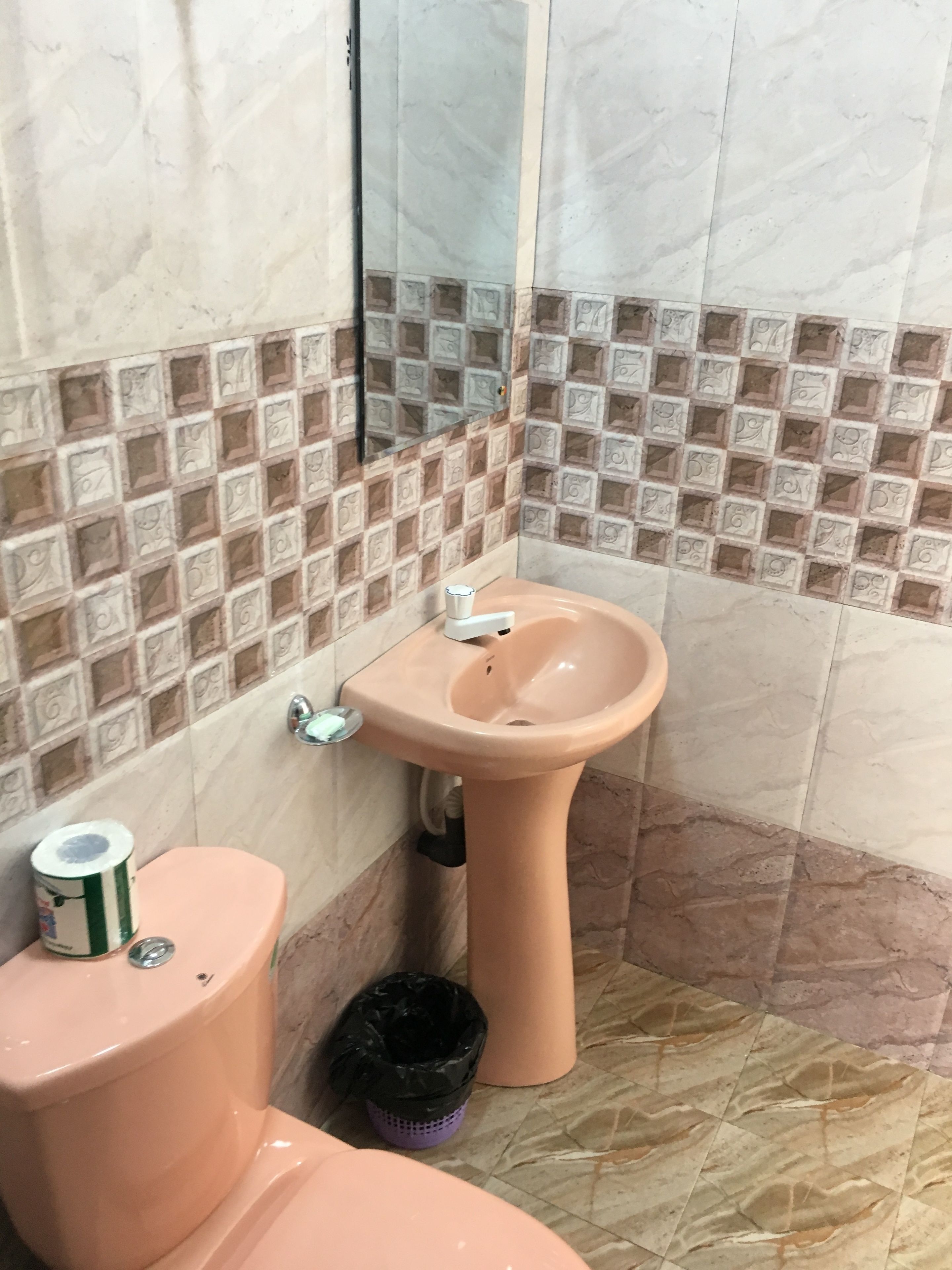 A bathroom with a pink toilet, a pink sink, and a black trash bin.