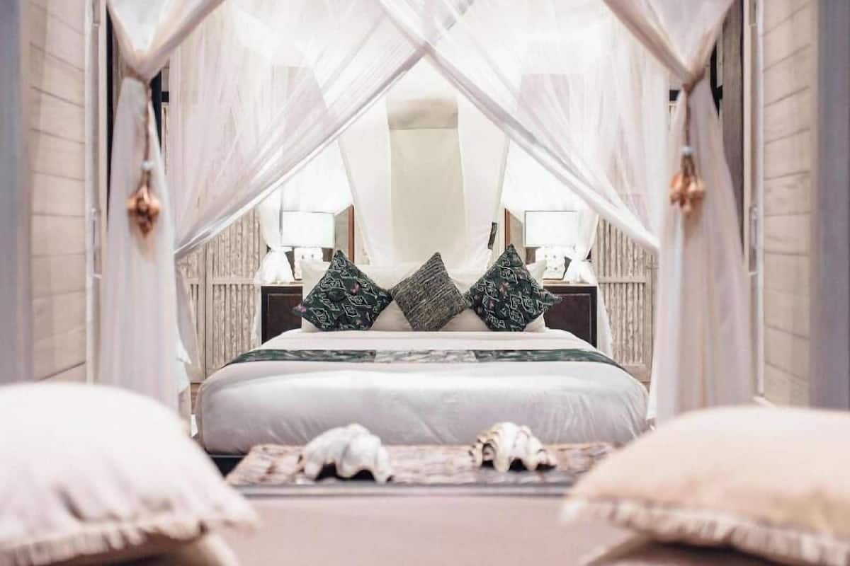 A bedroom with a canopy bed, bedside lamps, and decorative pillows.