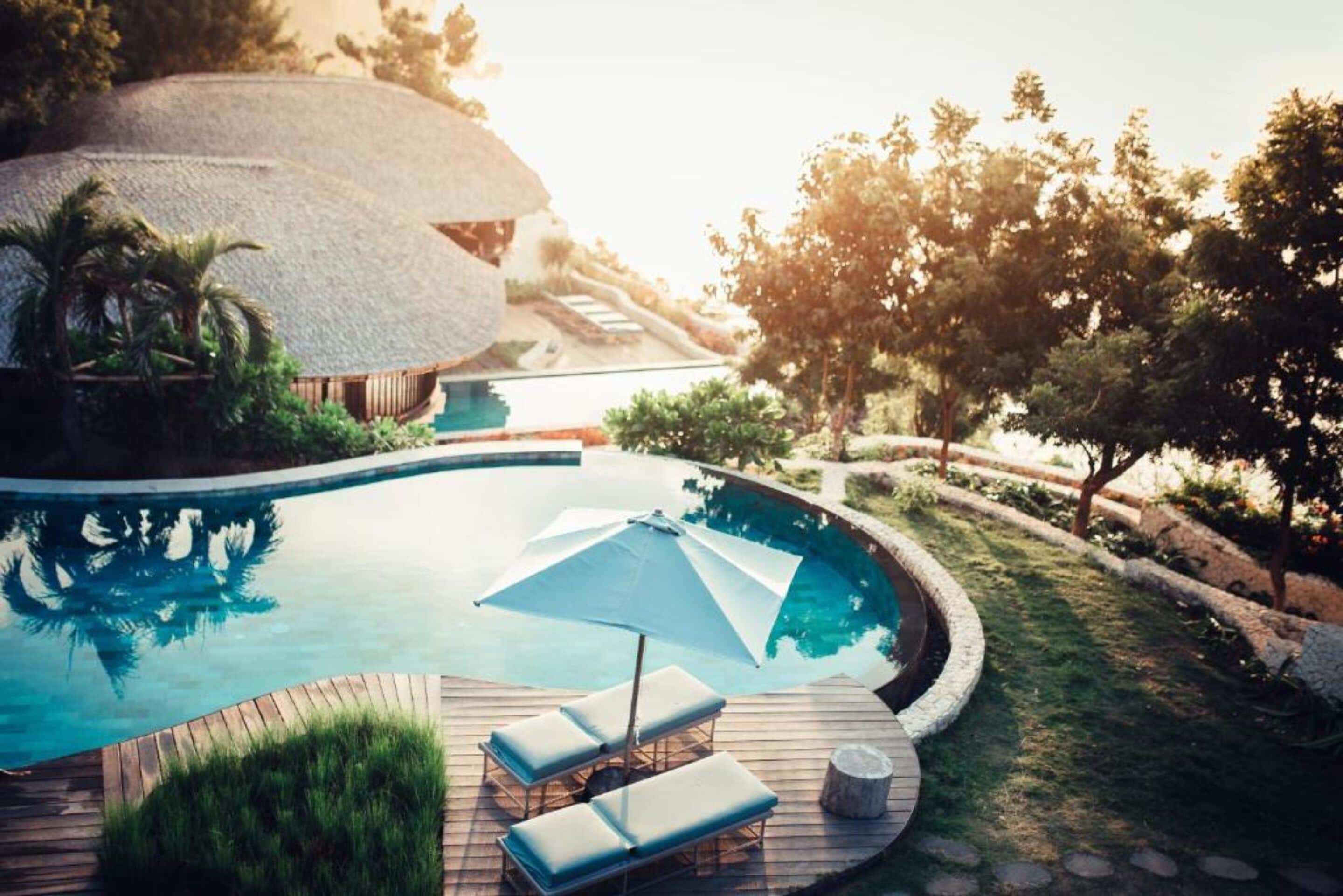 Una piscina con sillas de descanso y una sombrilla, rodeada de vegetación y un edificio de diseño en forma de cúpula.