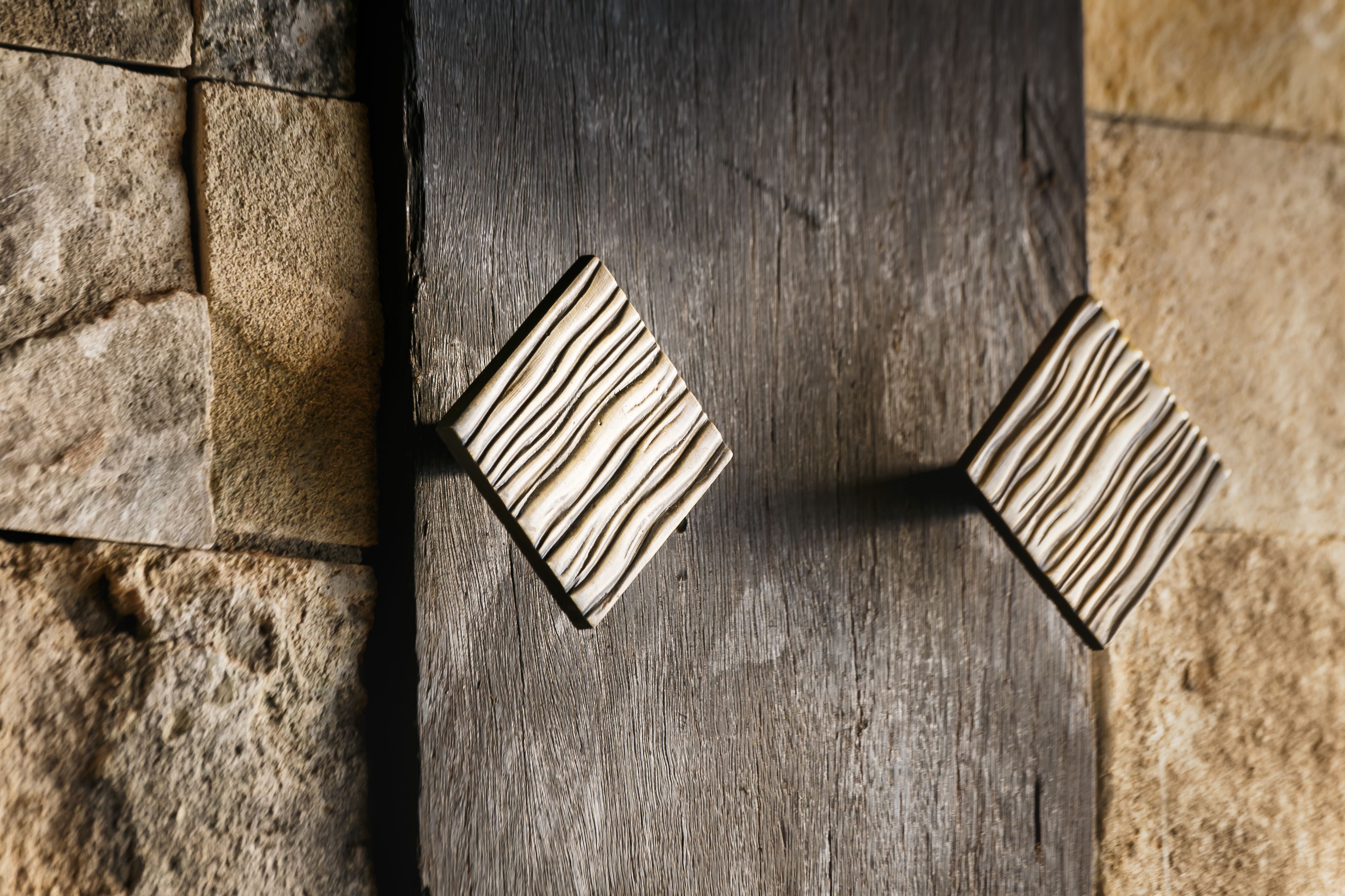 A close-up of a wooden door with a textured pattern and two square metal handles.
