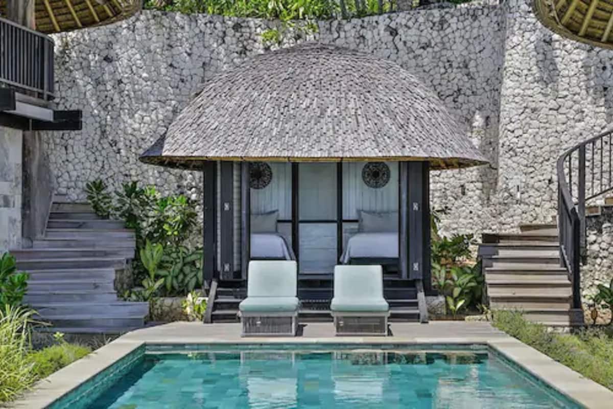 A pool area with a thatched roof seating area, stone walls, and a staircase.