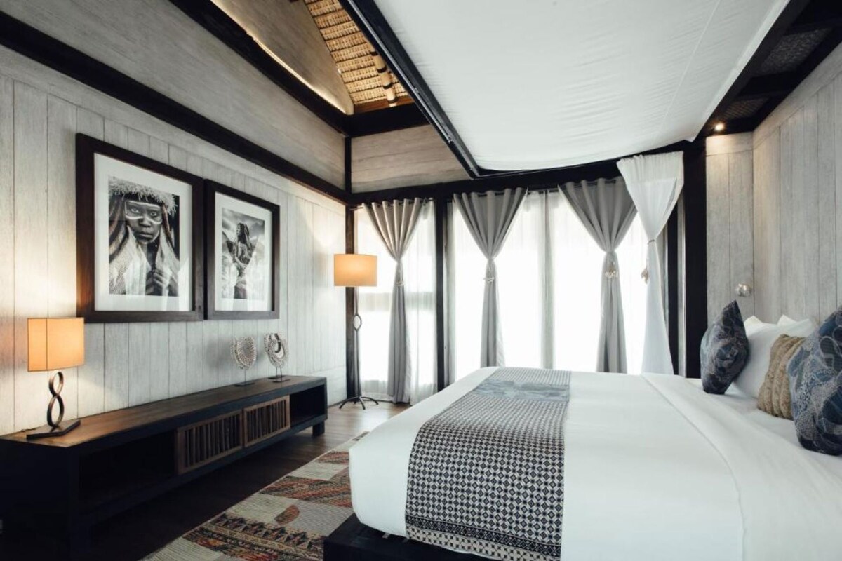 Una habitación de hotel moderna con una cama grande, una mesita consola y una lámpara de pie.