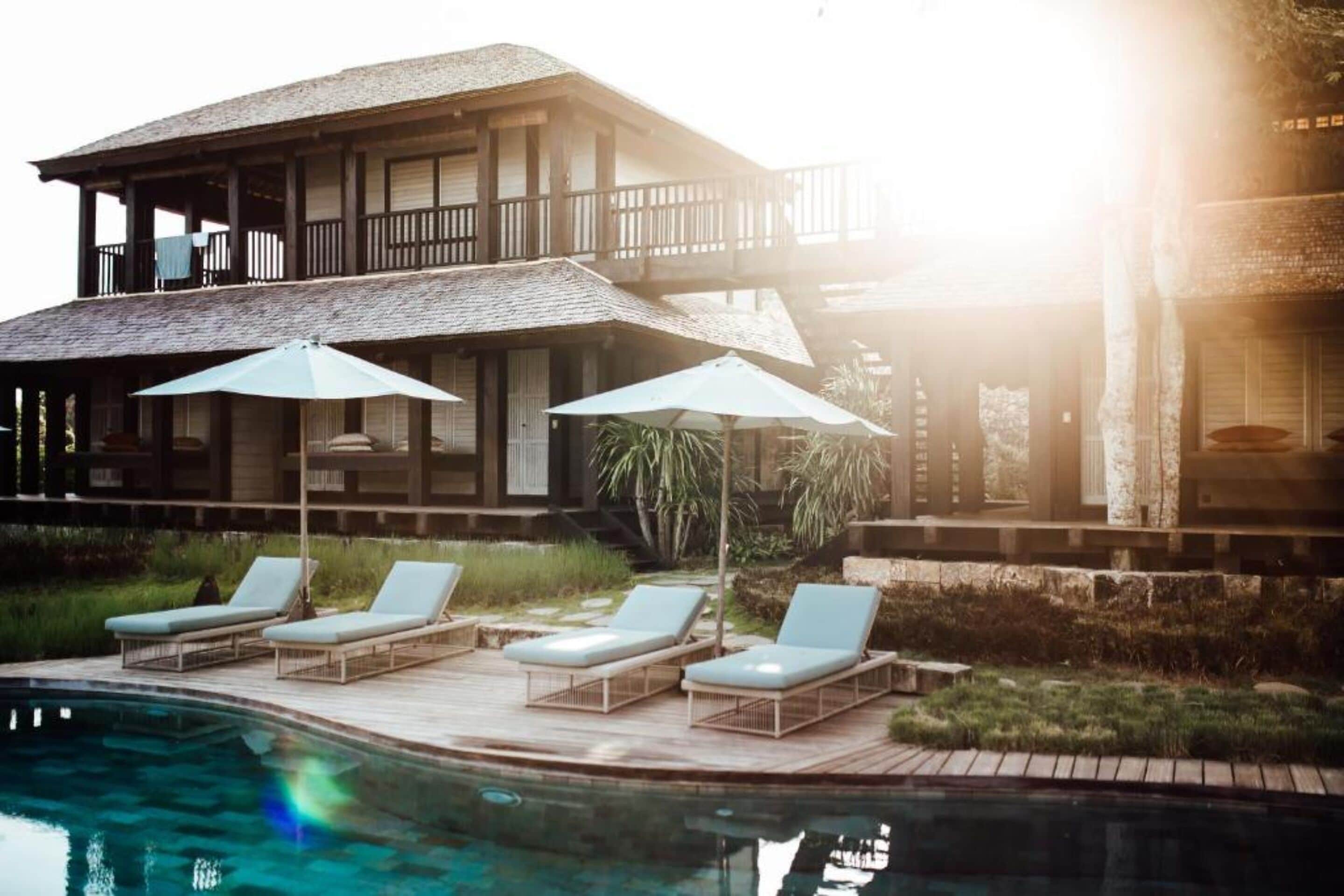 A pool area with lounge chairs and umbrellas, a wooden deck, and a building with a balcony.