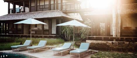 A pool area with lounge chairs and umbrellas, a wooden deck, and a building with a balcony.