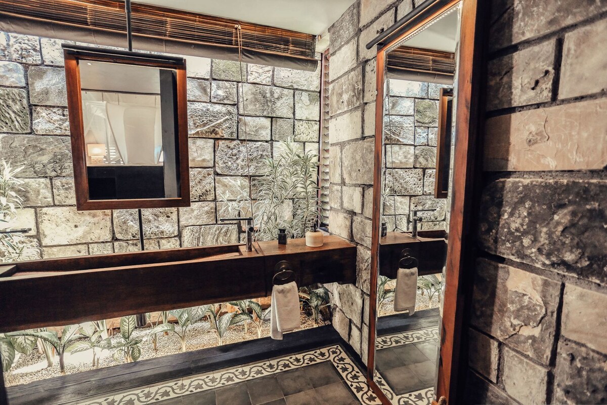 Un baño con pared de piedra, tocador de madera, espejo y perchero.