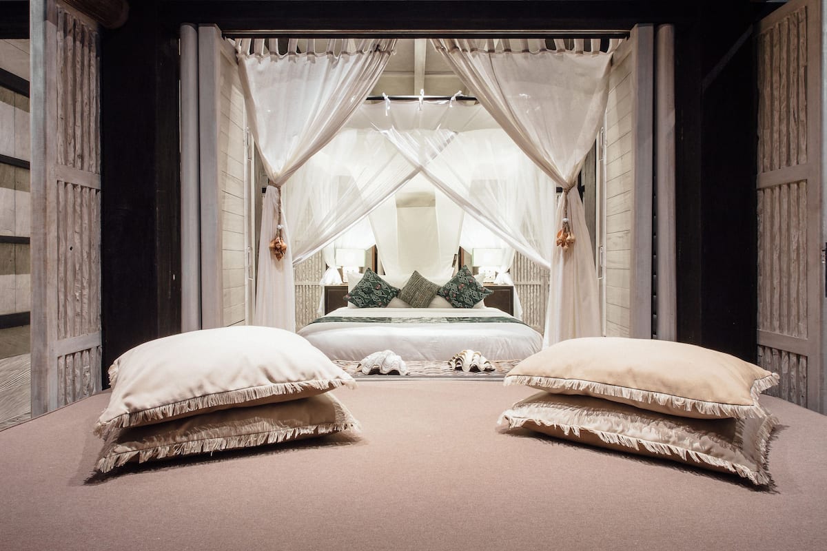 A bedroom with a canopy bed, two large pillows, and a nightstand with a lamp.