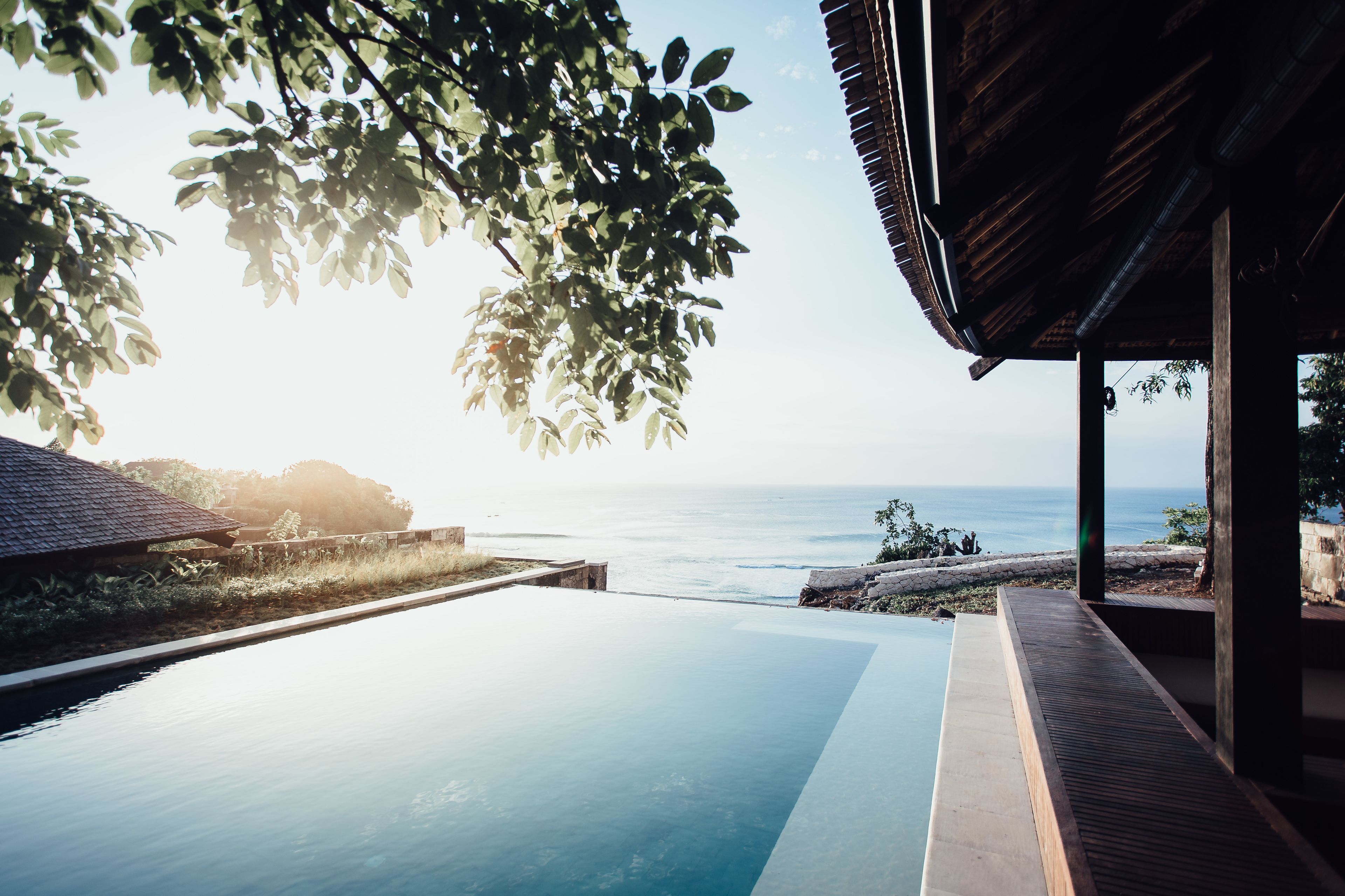 An infinity pool with a view of the ocean, wooden deck, and a covered area with a roof.