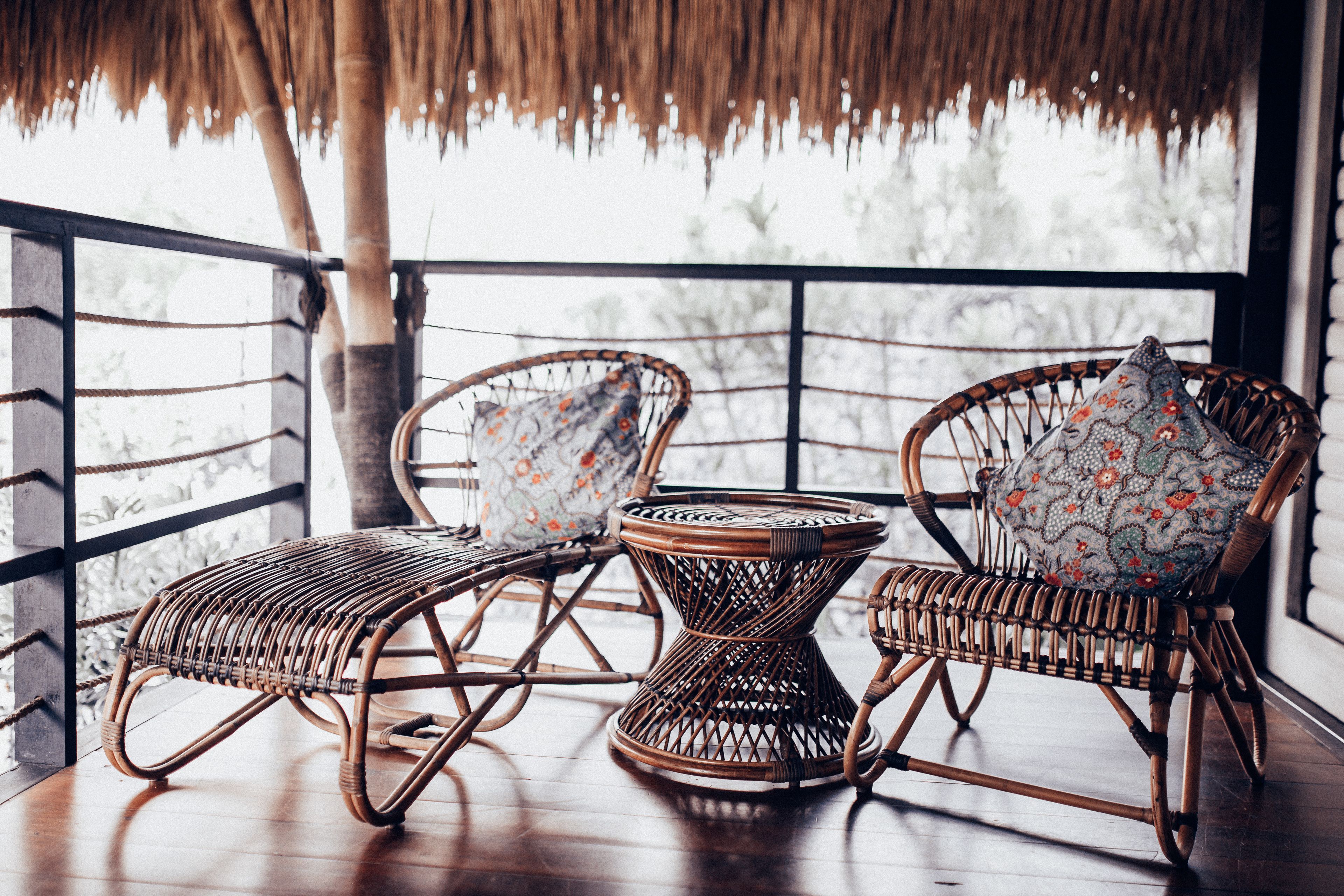Wicker furniture with patterned cushions on a wooden deck with a thatched roof.