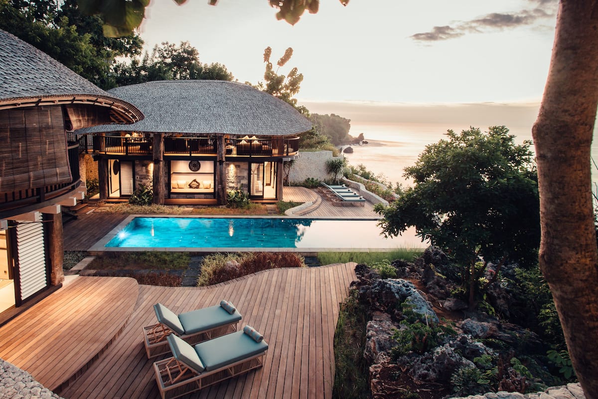 A luxurious villa with a swimming pool, wooden deck, and a view of the sea.