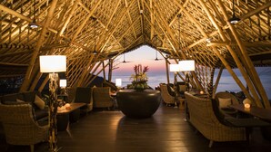 An open-air dining area with bamboo ceiling, wicker furniture, and a central table with a vase of flowers. - Suarga Padang Padang (Pecatu)