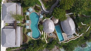 An aerial view of a resort with multiple swimming pools, connected by pathways, surrounded by lush greenery and a beach. - Suarga Padang Padang (Pecatu)