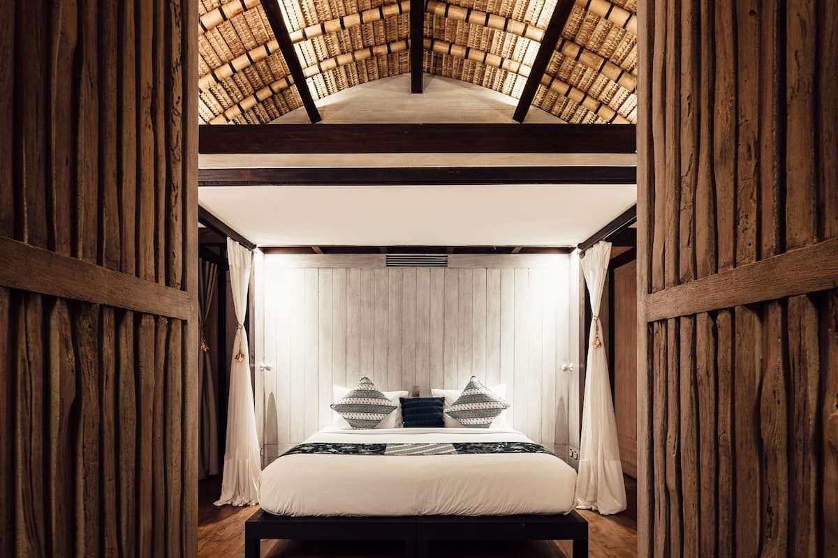 A room with a bed, wooden walls, and a woven ceiling.