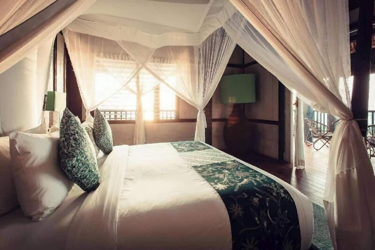 A bedroom with a canopy bed, a green patterned bedspread, and a view of the outside.